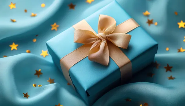 Blue gift box tied with a golden ribbon bow on blue satin fabric with small golden star confetti.