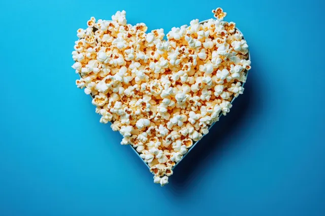 Heart-shaped popcorn bowl on blue background with crisp kernels and buttery specks