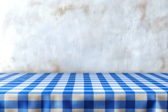 Empty table covered with a blue and white checkered tablecloth against a textured white wall.