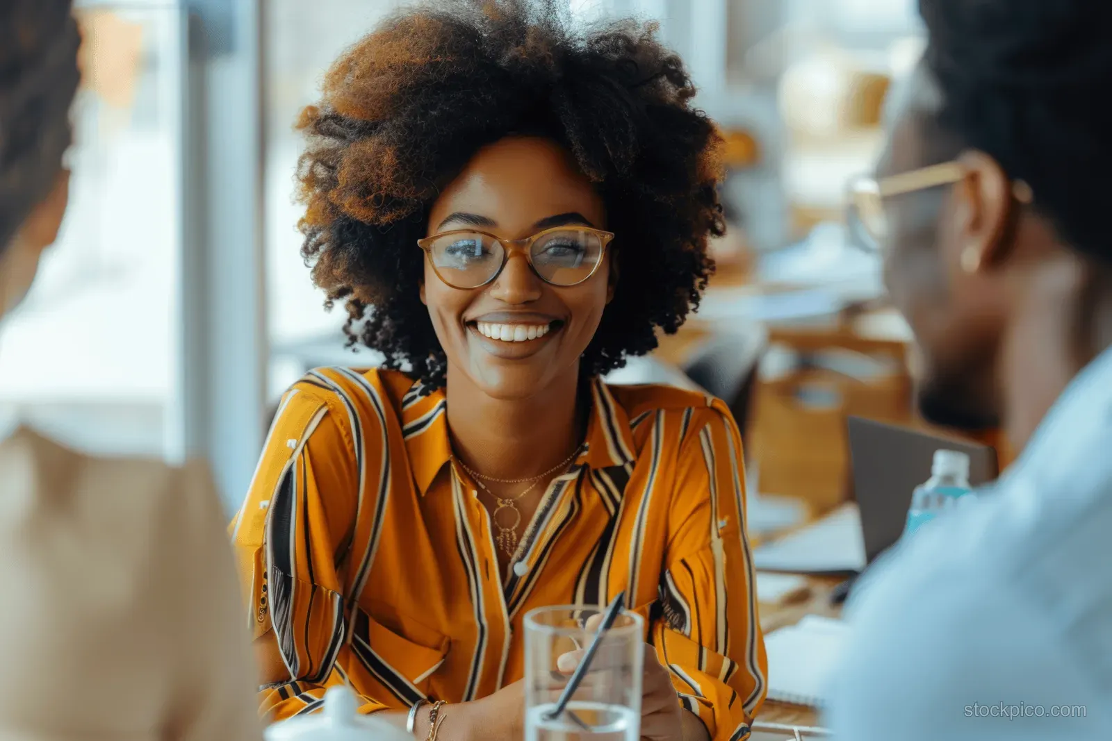 A smiling Black businesswoman leads a team discussion at a modern office conference table.
