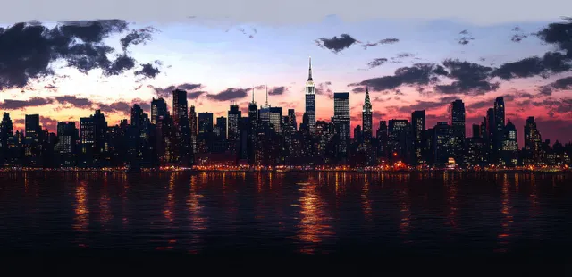 City skyline at dusk reflected on calm water under colorful clouds.