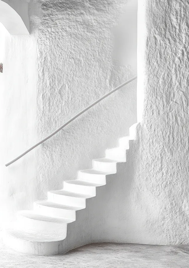 White curved staircase ascending beside textured walls with a simple handrail under bright natural light.