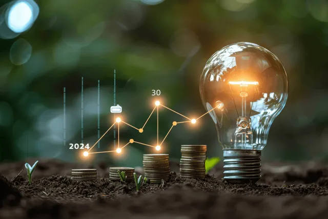 A glowing light bulb above stacked coins on soil with a rising 2024 line chart in the background.