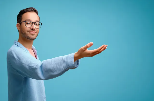Cheerful young businessman gesturing with open hand on clean blue background