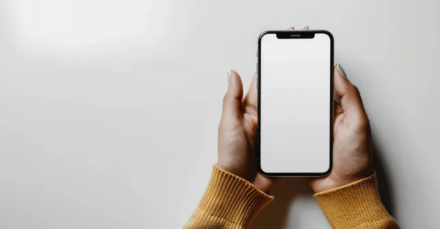 A woman holds a smartphone showing a blank white screen while typing with her hands visible.