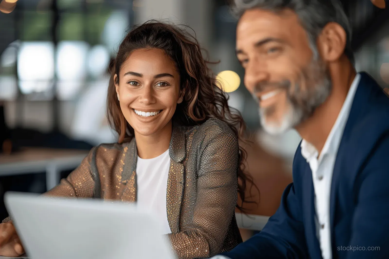 Smiling businesswoman reviews a laptop with a suited colleague during an office discussion.