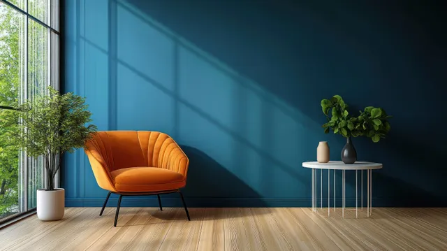 Orange armchair and small round table with a potted plant in a modern living room with a deep blue wall.