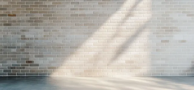 Empty interior corner with white brick wall and soft daylight casting long shadows over a smooth concrete floor.