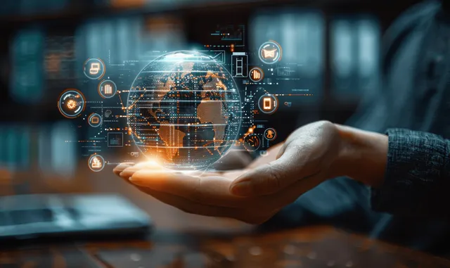 A hand holds a glowing holographic globe with education icons in front of a blurred classroom setting.