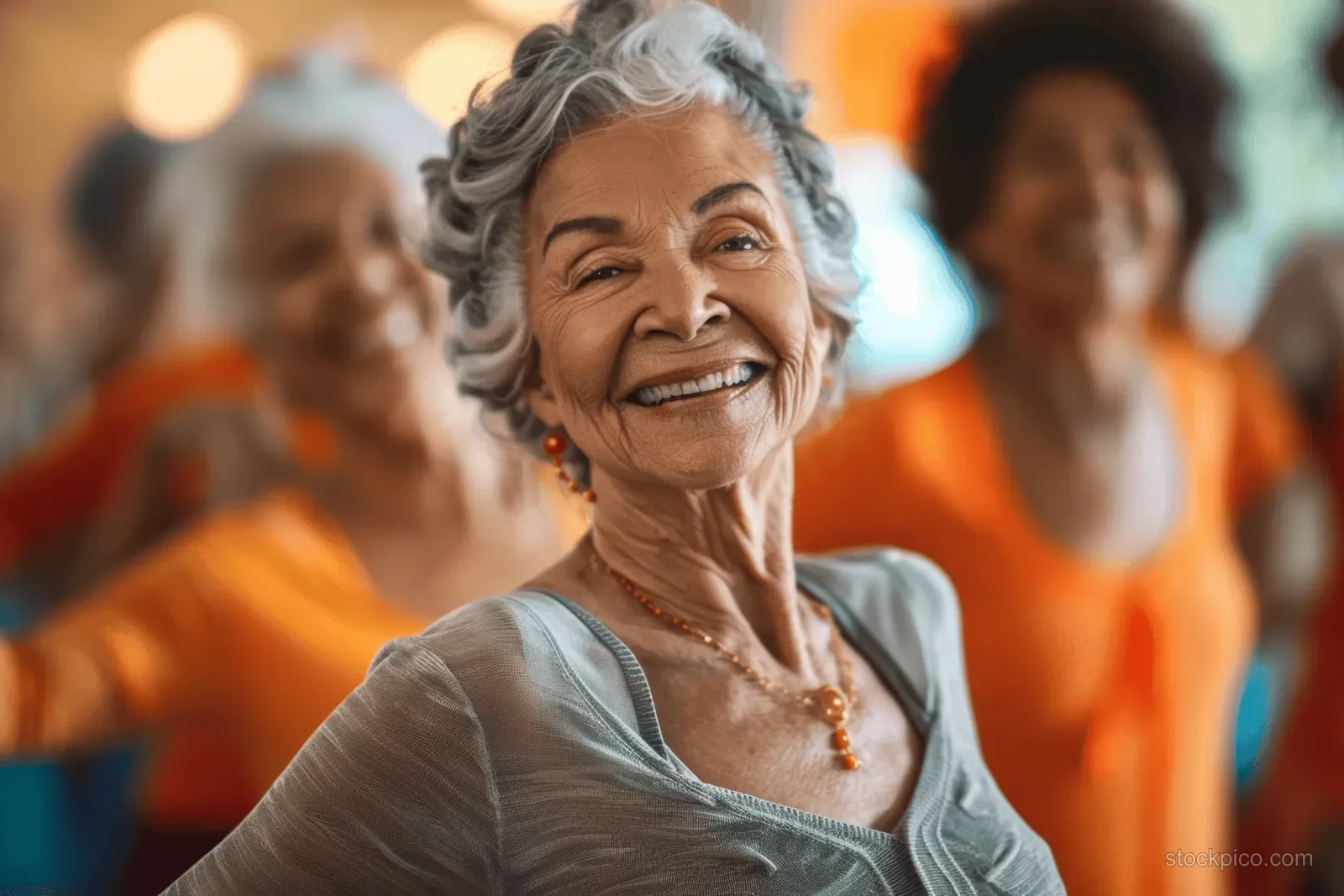 Elderly woman with gray hair smiles in the foreground during a lively community gathering with colorful people behind.