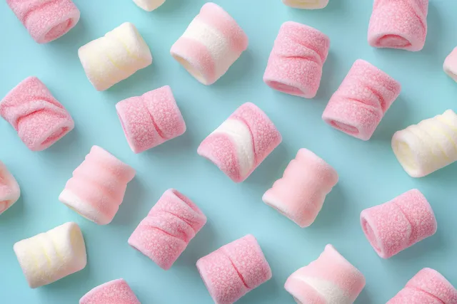 Pink and white marshmallows scattered on a light blue background with soft shadows.