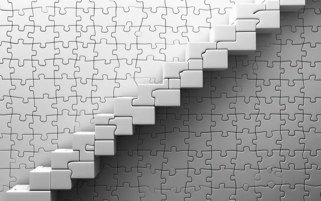 White puzzle pieces stacked into a step-like staircase on a table with scattered gray pieces beside them.