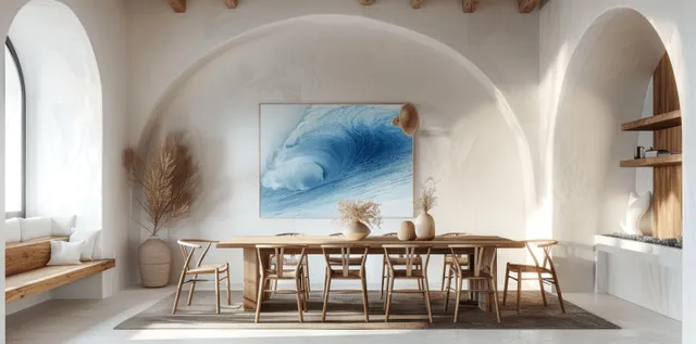 White coastal dining room with arched alcove, wooden table, chairs, and a blue sea landscape artwork on the wall.