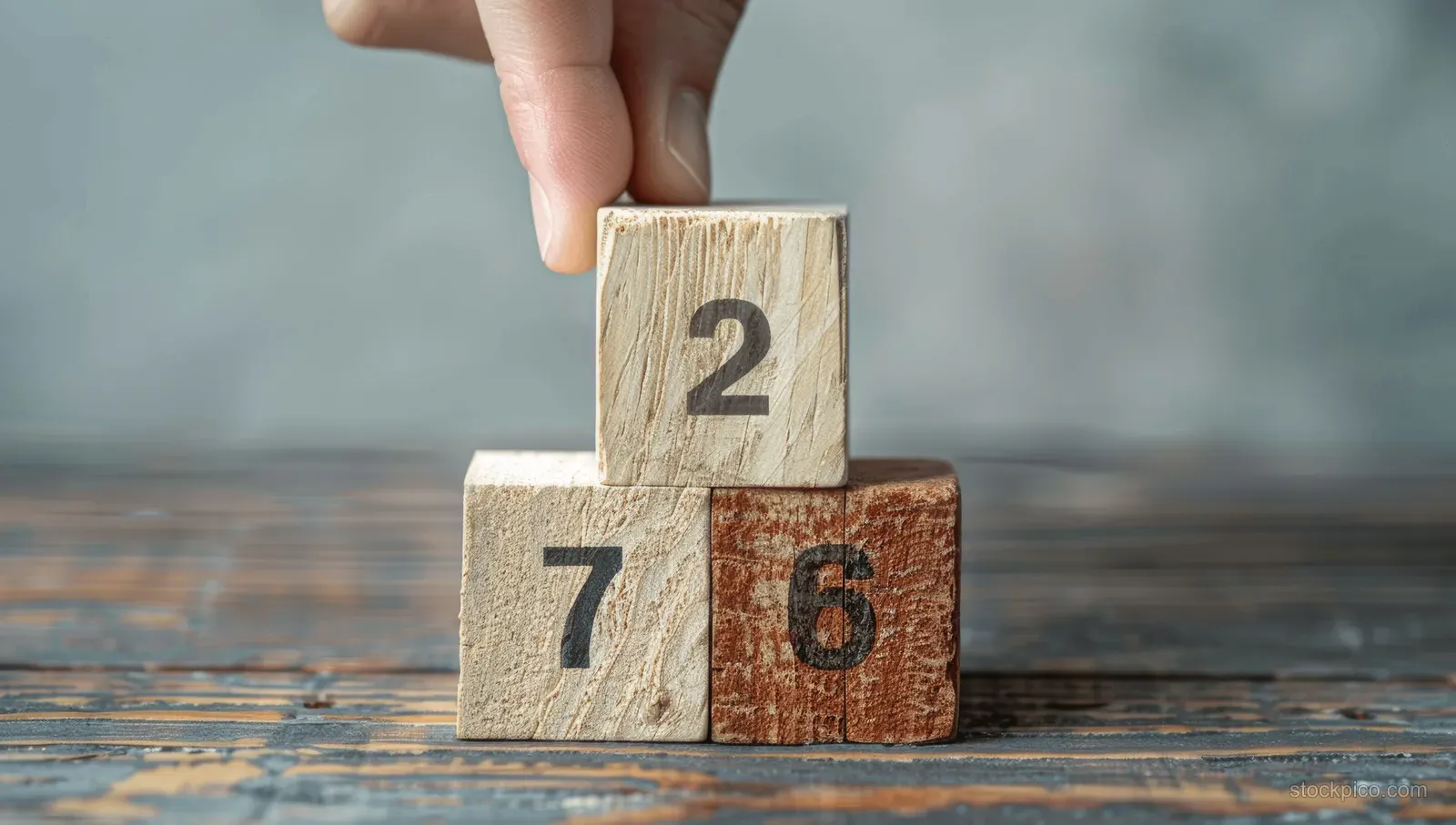 A hand stacks numbered wooden cubes on a table to show task prioritization and workflow steps.