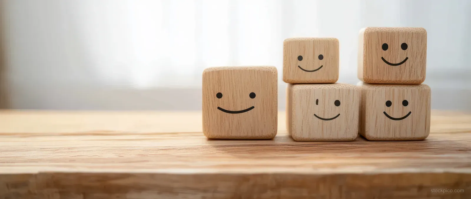 Wooden smile-face rating blocks stacked on a desk with a soft curtain background.