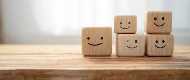 Wooden smile-face rating blocks stacked on a desk with a soft curtain background.