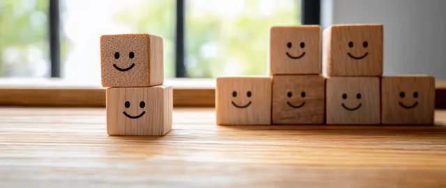 Smiley blocks stacked to show survey satisfaction growth on a wooden surface