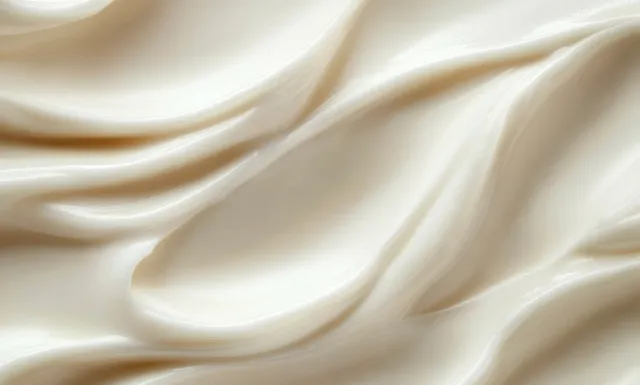 Creamy lotion swirls on a pale minimalist background with smooth glossy texture and soft highlights.