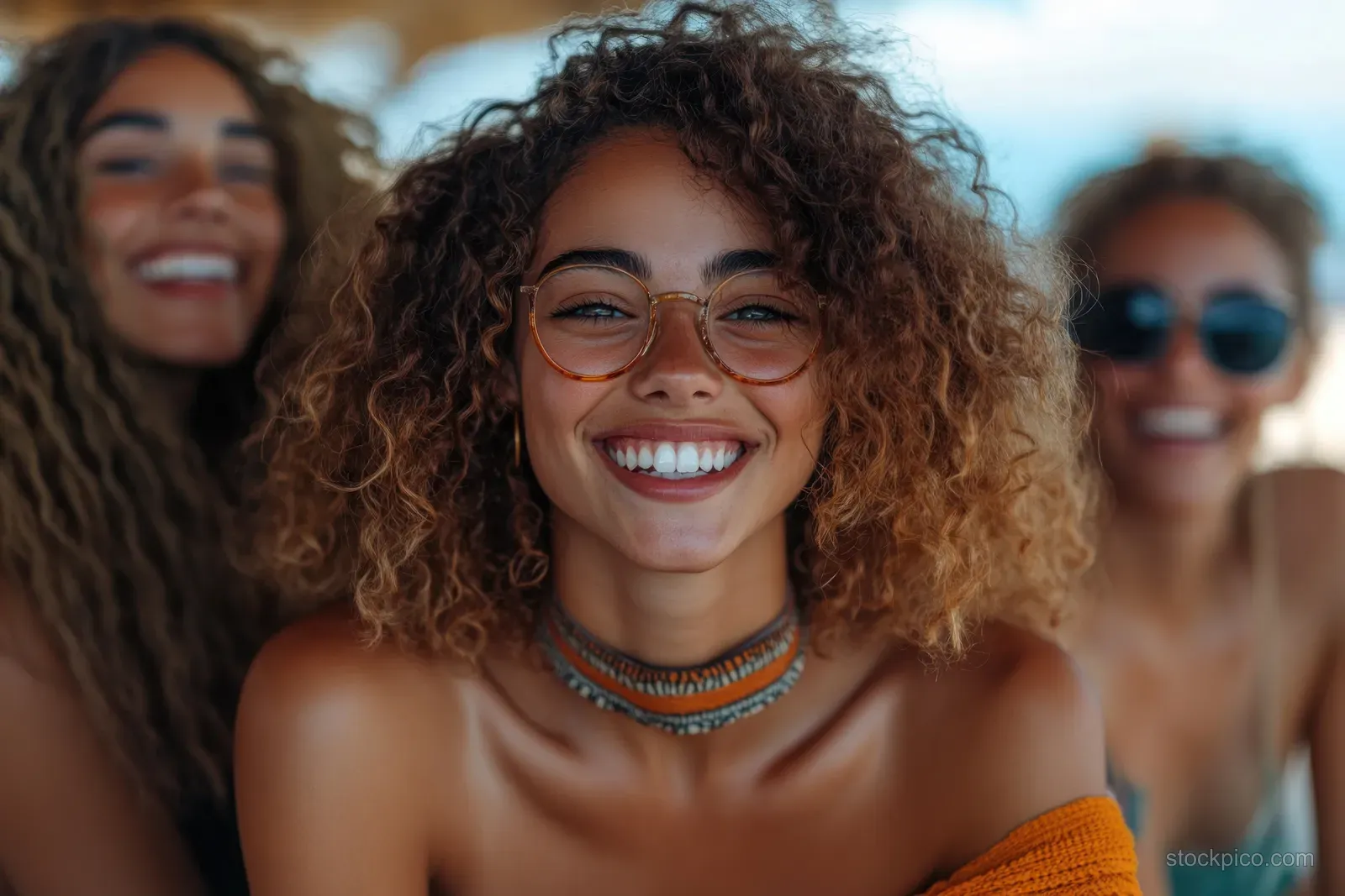 A young woman with curly hair smiles while friends laugh together outdoors in winter sunlight.