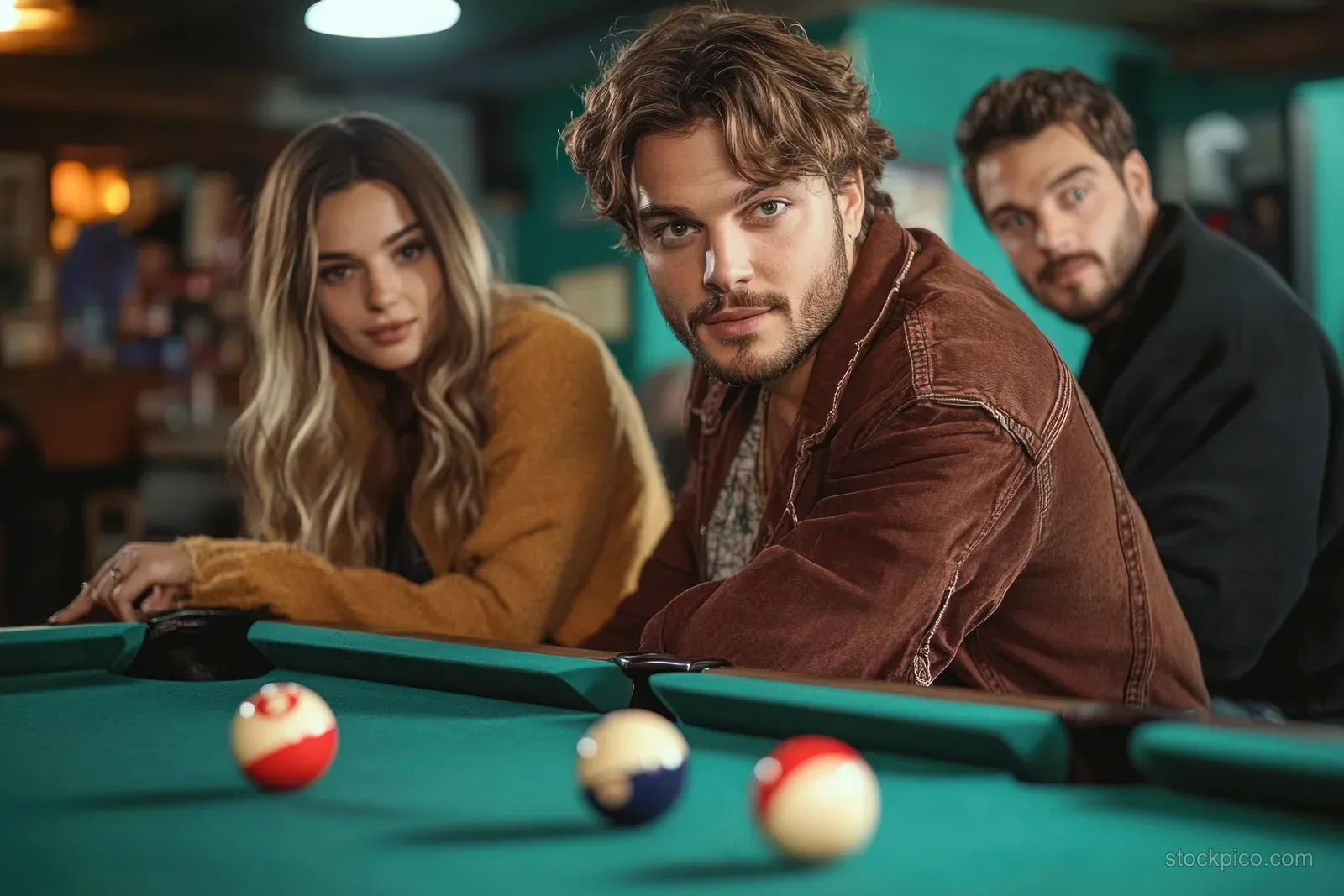Woman pool player aims the cue at a white ball while friends watch across green billiard tables in an indoor bar.