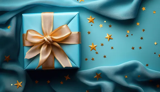 Blue gift box tied with golden ribbon on teal fabric, scattered star confetti