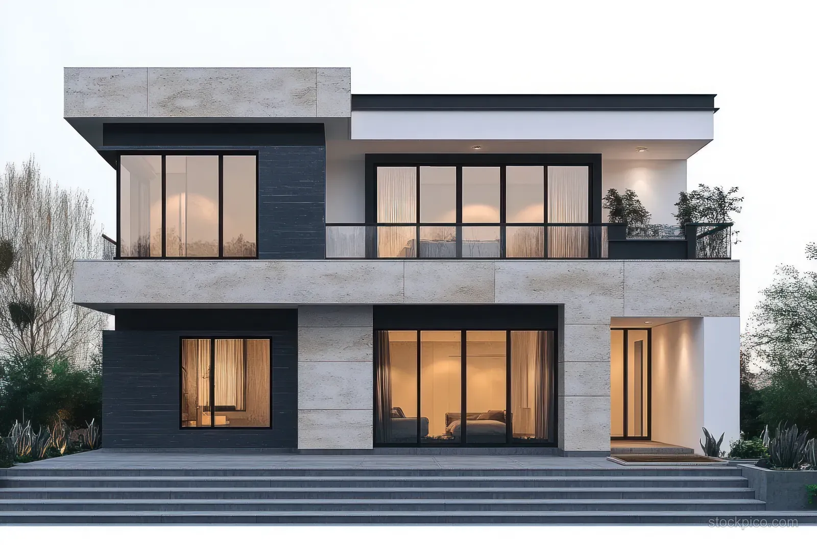 Two-story modern house exterior at dusk with large glass windows, balcony, and warm lights beside landscaped greenery.