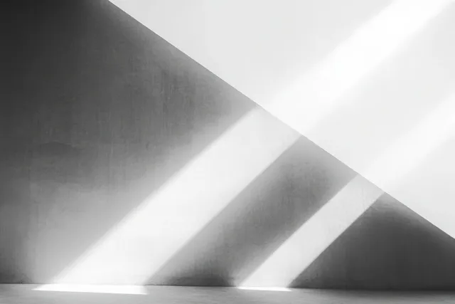 Diagonal black and white light beams cast geometric shadow bands on a textured interior wall.