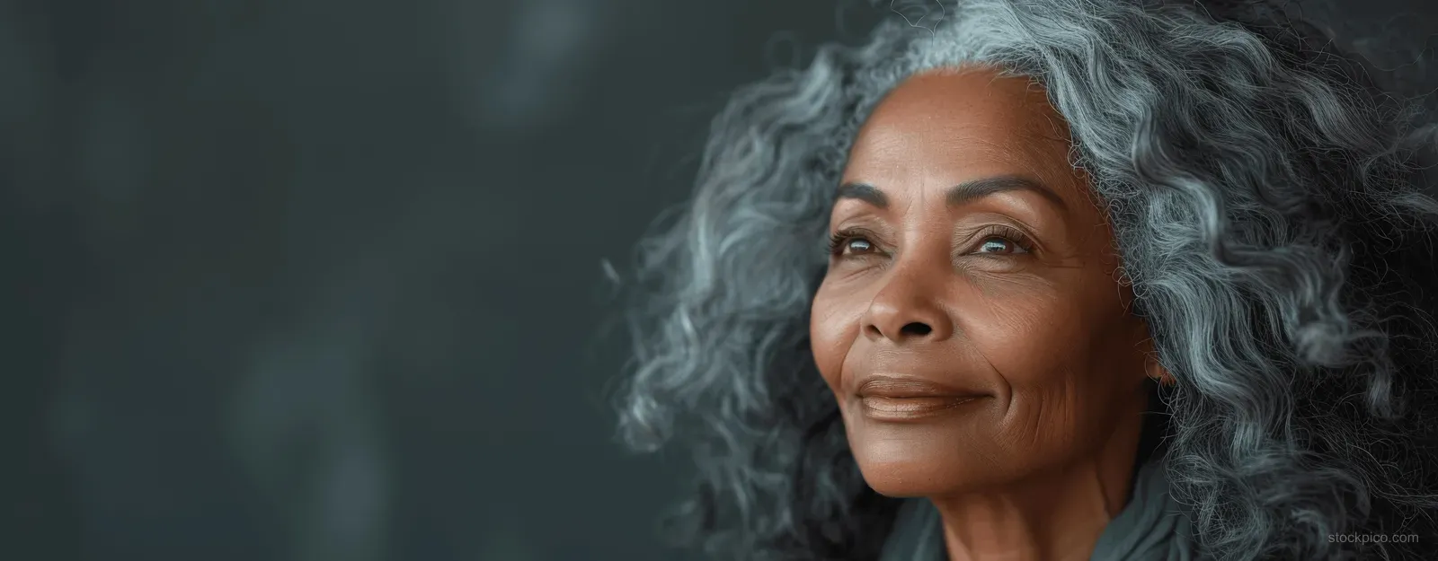 Smiling senior Black woman with long curly gray hair in a studio portrait under soft cinematic lighting.
