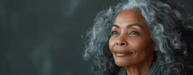 Smiling senior Black woman with long curly gray hair in a studio portrait under soft cinematic lighting.