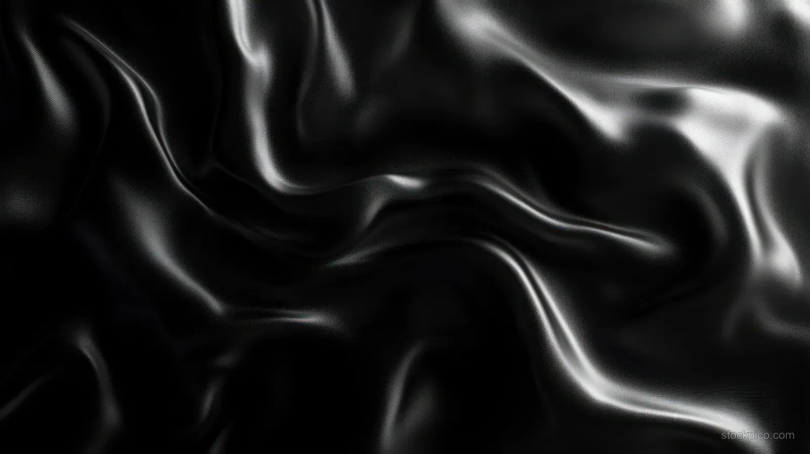Close-up of black silk fabric with glossy highlights and flowing soft folds forming ripples.