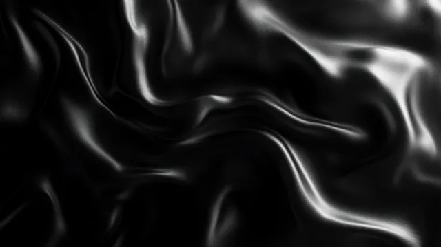 Close-up of black silk fabric with glossy highlights and flowing soft folds forming ripples.
