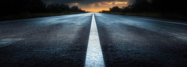 A wet highway at twilight with reflective asphalt and glowing white lane lines stretching toward the horizon.