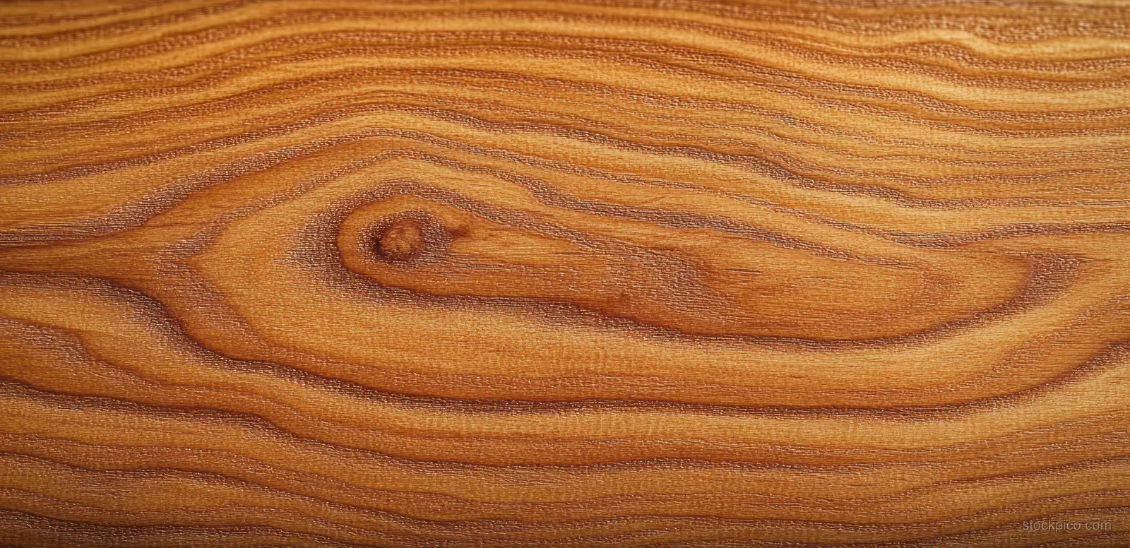 Close-up cherry wood grain texture with swirling growth rings in warm amber and brown tones.