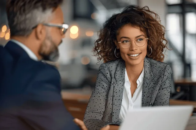 Curly-haired businesswoman discusses project with colleague across laptop in office meeting