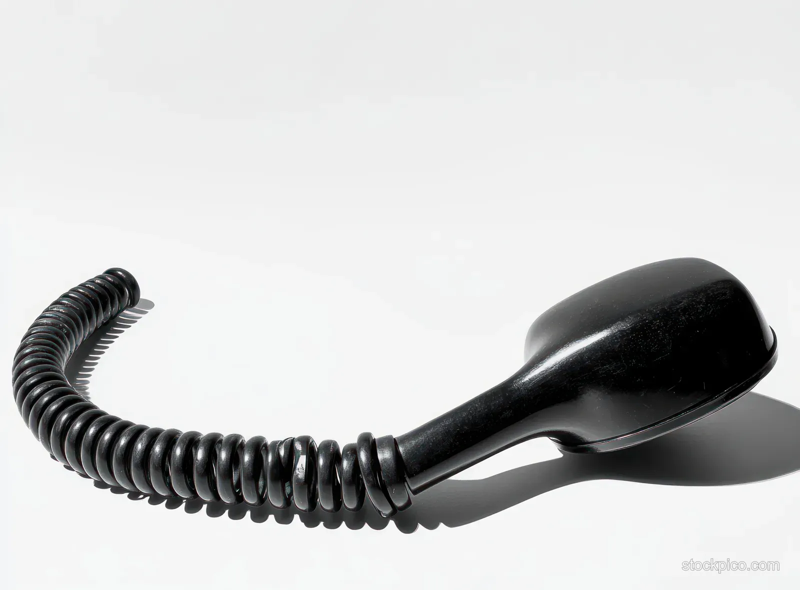 A black telephone handset with a coiled cord rests on a white surface, casting a sharp shadow.