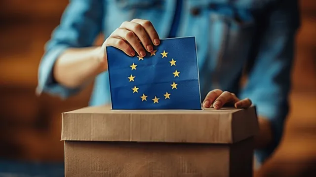 A woman’s hands place a blue EU-starry card into a ballot box on a wooden pedestal.