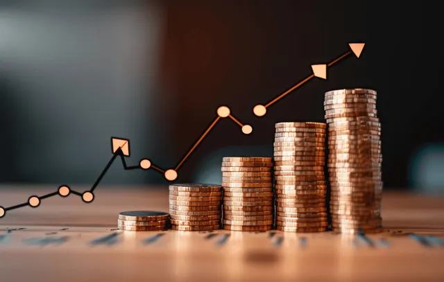 Stacked Coins Rising Beside Upward Market Chart on Desk