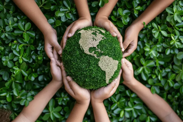 Children hold a grass-covered Earth globe together while standing around a ring of green leaves.