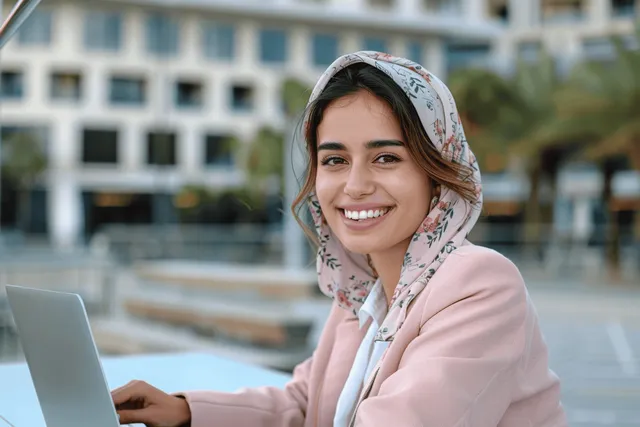 Smiling young businesswoman working on a laptop outdoors near modern architecture