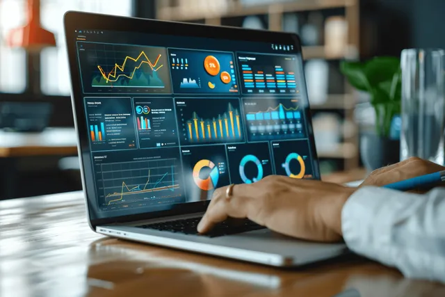 Hand holding a touch pen over a laptop displaying analytics dashboards, growth graphs, and KPI charts in an office.