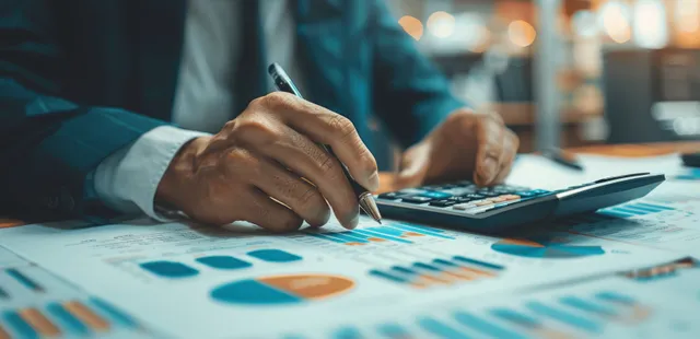 Businessman hand writing on a financial spreadsheet with calculator and documents on a desk in an office.