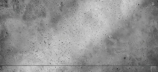 Gray concrete wall close-up with dark speckles, small holes, rough texture, and a faint horizontal seam near the bottom.