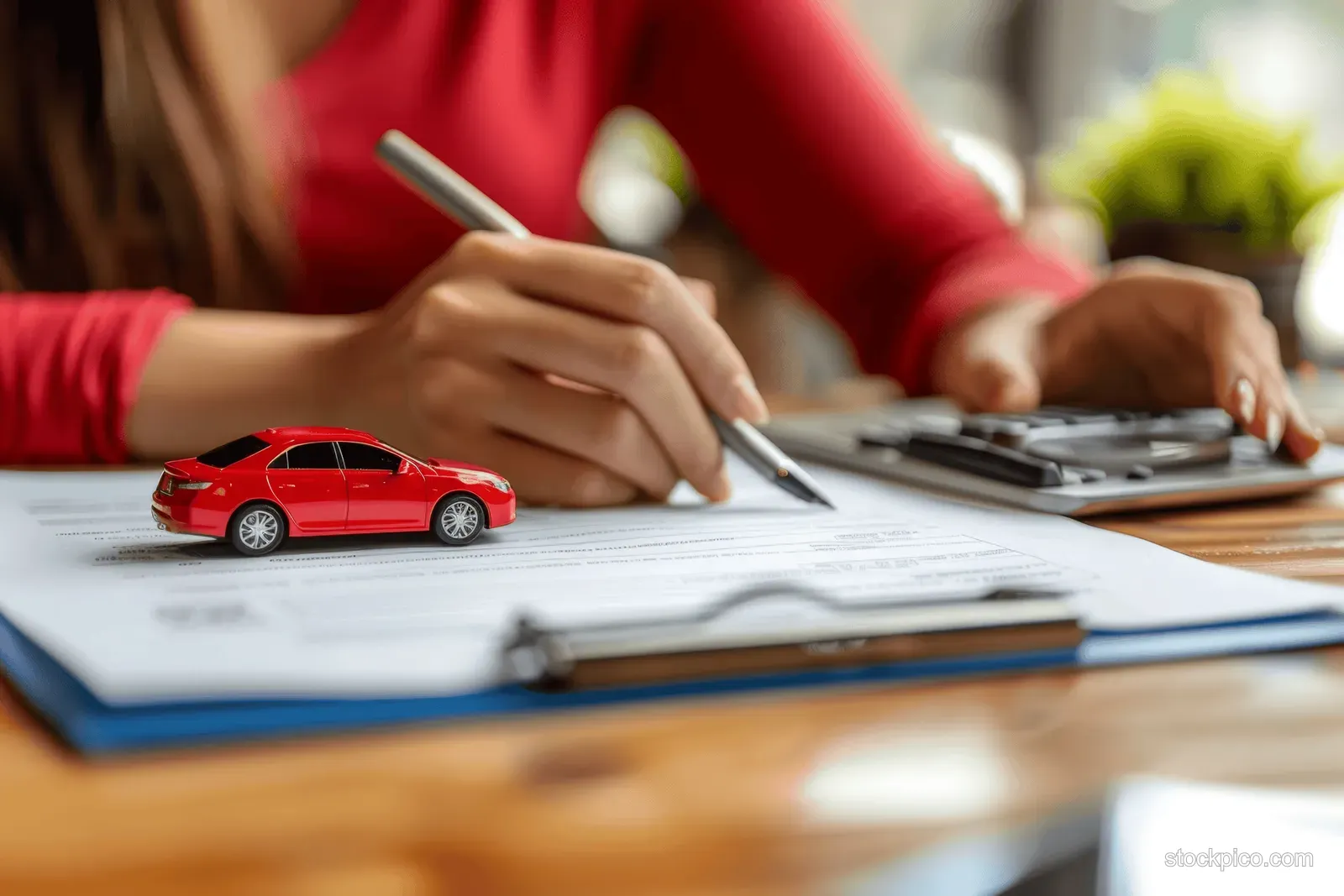 A woman signs car insurance and lease paperwork while a small red sedan model sits on the desk.