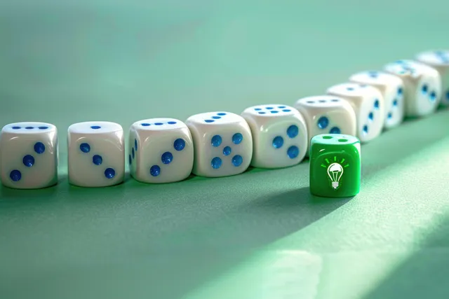 A green die with a glowing light bulb icon stands out among white dice with blue dots on a green surface.
