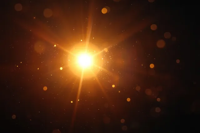 A glowing golden light orb emits radiant beams with scattered sparkling particles against a dark background.
