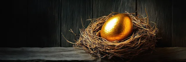 A golden egg sits in a straw nest on a wooden table with a dark backdrop.