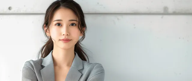 Reflective young Japanese businesswoman in gray suit, thoughtful expression against white office wall