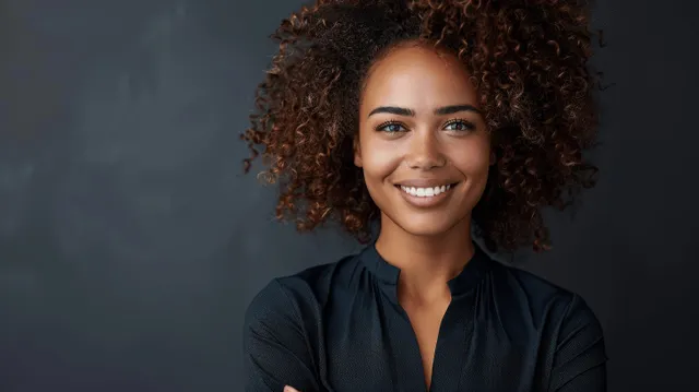 Smiling businesswoman with curly hair in black blouse against a muted grey studio background