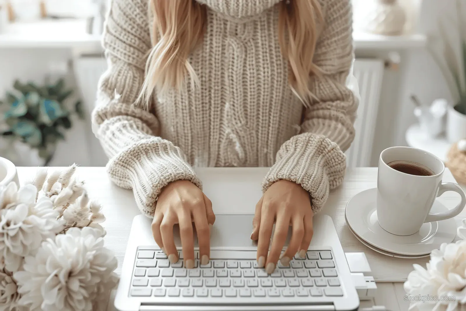 Woman typing on a laptop at a desk beside a coffee cup in a softly lit office setting.