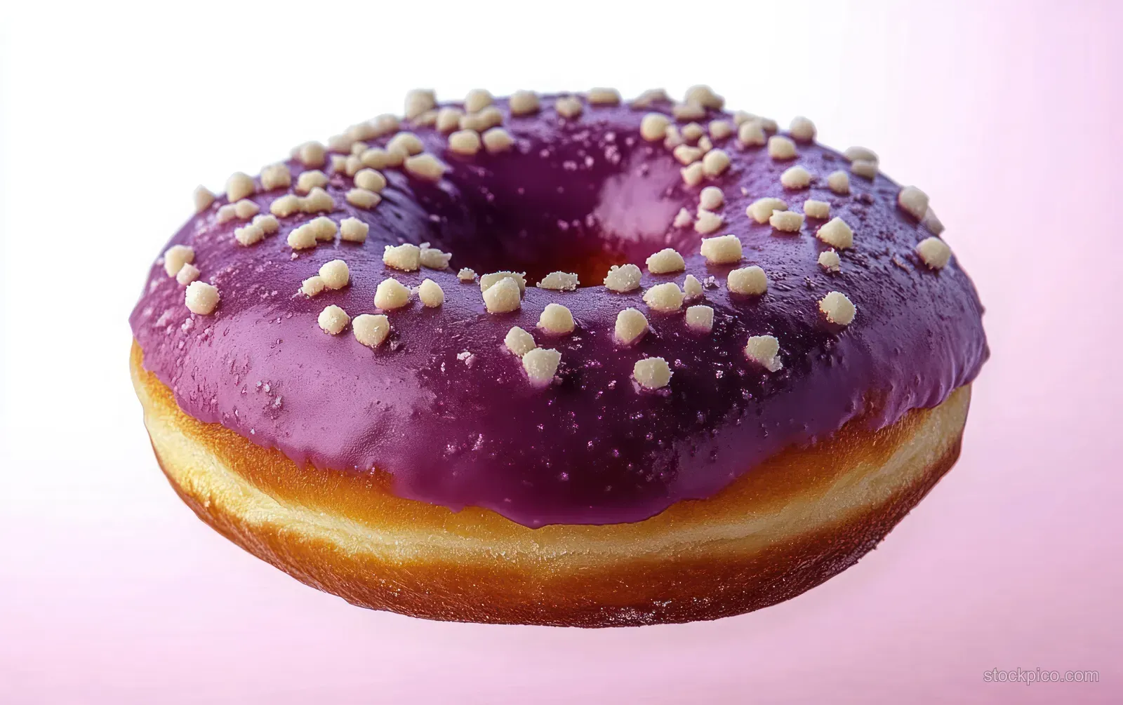 A glazed doughnut with purple icing and white sprinkles against a soft pink background.